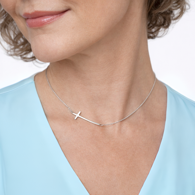 Silver necklace with a cross pendant worn by a person in a light blue top.