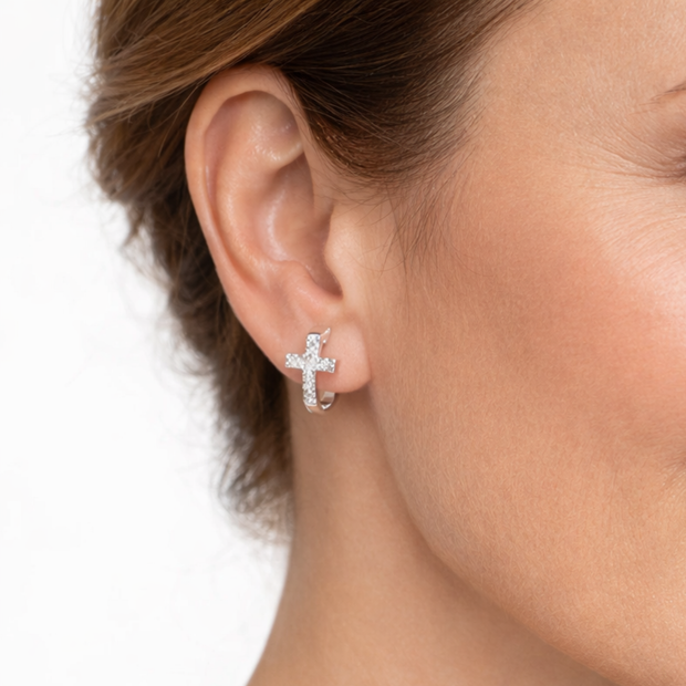 Close-up of an ear wearing a silver cross earring on a white background